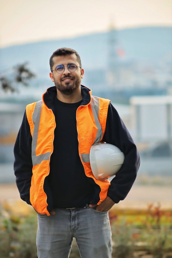 services-03 Confident male construction worker with safety vest and hard hat in a blurred outdoor setting.