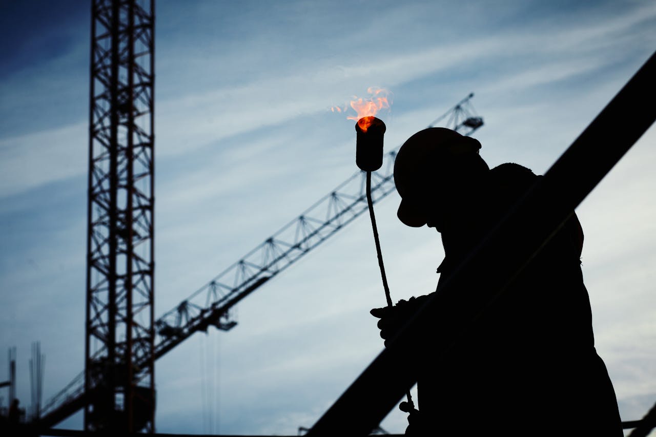 services-01 Silhouette of a construction worker using a blowtorch at a building site against a crane-filled skyline.